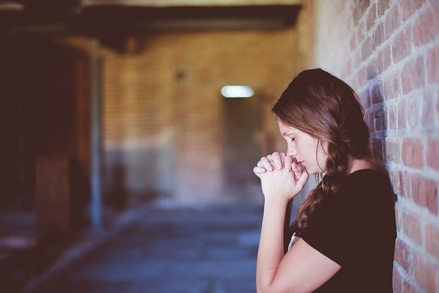 Teen girl leaning against a brick wall praying